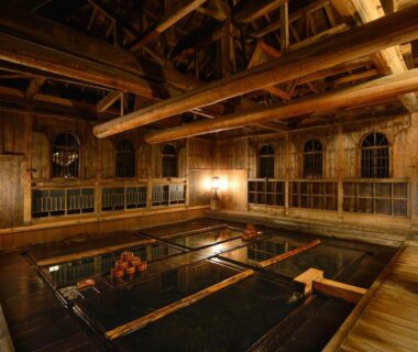 Large wooden communal onsen bath with high beams and lantern lighting at Houshi Onsen Chojukan, Gunma