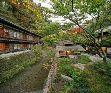 Wooden riverside ryokan buildings along a stream at Houshi Onsen Chojukan in Gunma Kanto