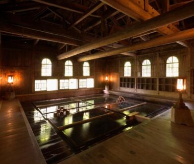 Wooden indoor onsen bath with high beams and arched windows at Houshi Onsen Chojukan, Gunma
