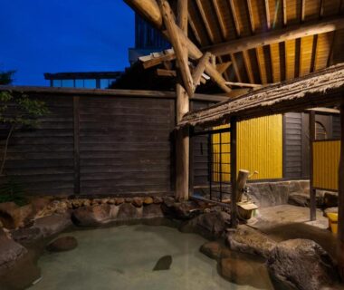 Stone-lined outdoor onsen with wooden shelter and sliding doors at Hozanso Beppu, Oita