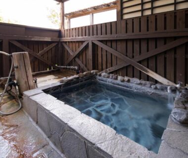 Enclosed outdoor stone onsen tub with wooden fence and hand shower at Hozanso Beppu, Ōita