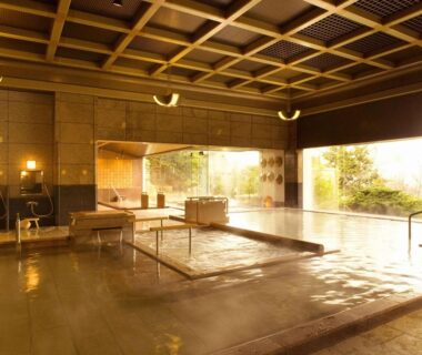 Spacious indoor onsen bath with stone floor, wooden coffered ceiling and large windows overlooking a garden at Hyoe Koyokaku Hyogo