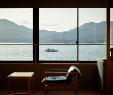Seating area with low table and chairs facing large window overlooking bay and mountains at ITSUKUSHIMA IROHA Hiroshima