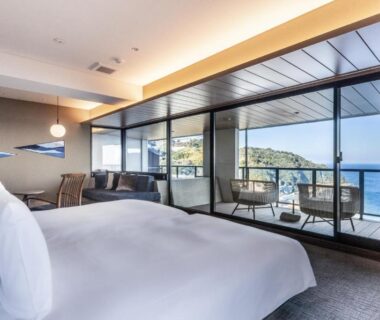 Large bed and seating area with balcony overlooking coastline at IZU RETREAT by Onko Chishin, Shizuoka