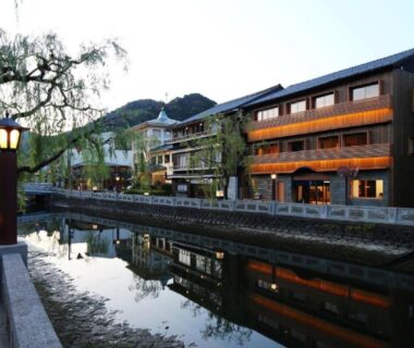 Riverside ryokan buildings lit at dusk with willow trees and reflections in canal at Ichidaya, Hyōgo Japan