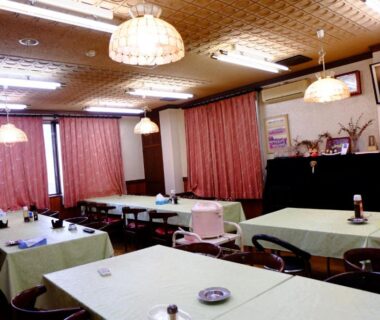 Communal dining hall with long covered tables, pendant lights, curtains and wooden accents at Ichifujiso, Yamanashi