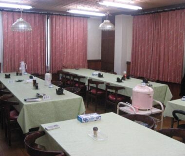 Long communal dining hall with tables, chairs, place settings and a pink hot water urn at Ichifujiso Yamanashi