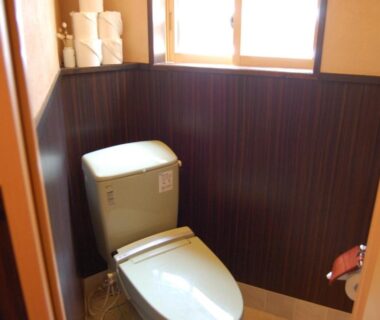 Compact restroom with modern toilet, wooden wall panels and small window at Ichinokurasou Nagano