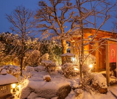 Snow-covered stone lanterns and lantern-lit path leading to Ichinomatsu Japanese Modern Hotel entrance in Gifu