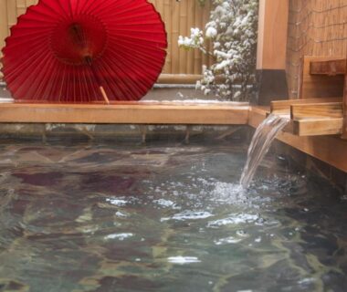 Wooden onsen bath with flowing spout and red paper umbrella at Ichinomatsu Japanese Modern Hotel, Gifu, Chūbu