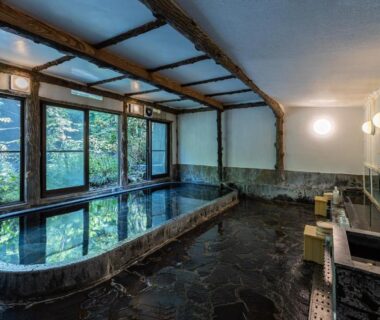 Traditional indoor onsen with stone bath, wooden beams and garden-view windows at Ichinoyu Honkan, Kanagawa