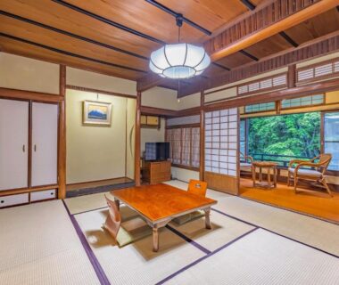 Traditional tatami room with low table, shoji screens and window seating overlooking greenery at Ichinoyu Honkan, Kanagawa