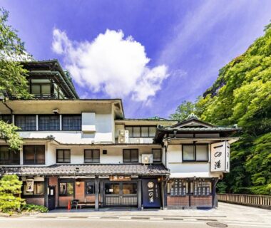 Multi-story ryokan facade with entrance and greenery at Ichinoyu Honkan in Kanagawa