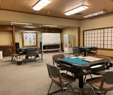 Mahjong game room with four tables, chairs, shoji screens and calligraphy scroll at Ichinoyu Honkan in Kanagawa