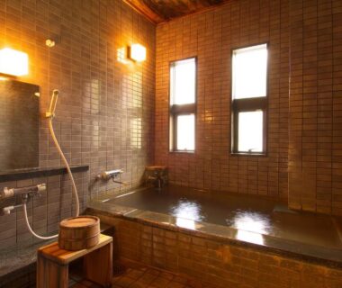 Tiled indoor onsen bath with wooden soaking tub and shower area at Ichinoyu Katei, Nagano