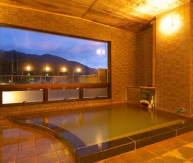 Tiled indoor onsen with large window showing mountain silhouettes at dusk, Ichinoyu Katei, Nagano