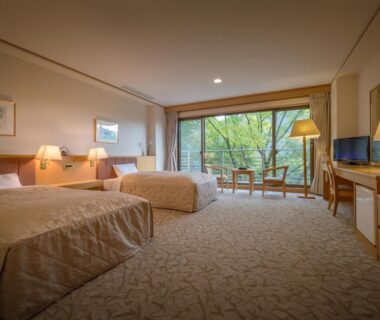 Twin beds, seating area and balcony overlooking greenery at Iizaka Onsen Surikamitei Ohtori, Fukushima