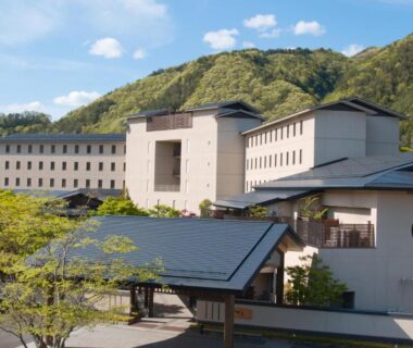Large ryokan building with tiled roof and mountain backdrop at Iizaka Onsen Fukushima