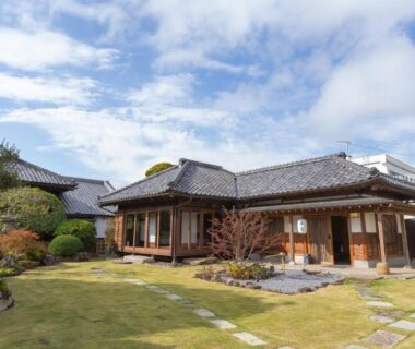 Single-story wooden ryokan with manicured lawn courtyard, stone path and traditional veranda at Iizukatei in Tochigi