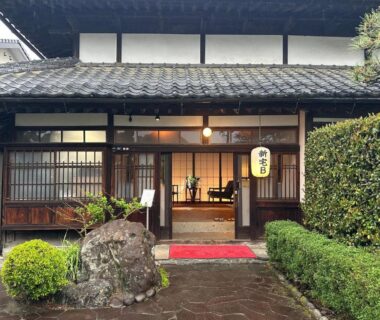 Wooden lattice entrance with stone path, lantern, and red mat at Iizukatei ryokan in Tochigi