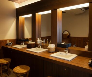 Three washbasins with wooden counter, mirrors and stools in a ryokan vanity area at Ijika Daiichi Hotel Kagura, Mie