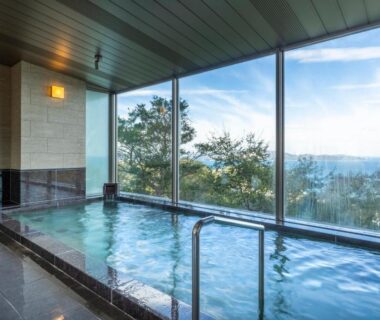 Indoor onsen bath with large glass windows overlooking coastal scenery at Ijika Daiichi Hotel Kagura, Mie, Kansai