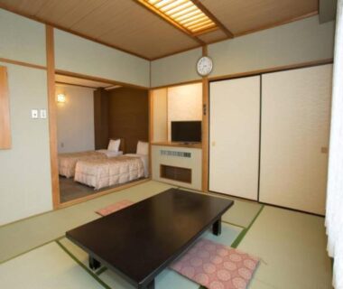 Tatami room with low table and adjacent sleeping area with beds at Ikaho Grand Hotel, Gunma
