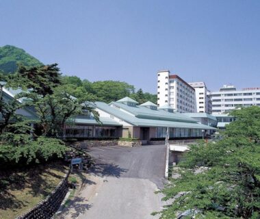 Hotel complex with sloped roofs and driveway among trees at Ikaho Grand Hotel in Gunma
