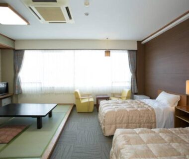 Room interior with tatami seating area, low table, twin beds and window armchairs at Ikaho Grand Hotel, Gunma