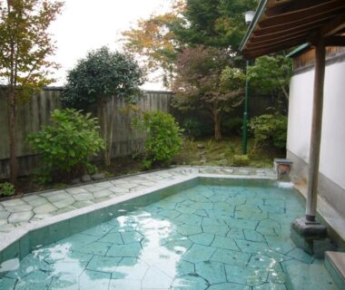 Stone-tiled outdoor onsen bath beside garden at Ikaho Grand Hotel Gunma