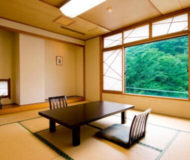 Traditional tatami room with low table, floor chairs, shoji screens and leafy forest view through window