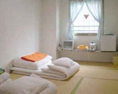 Simple tatami room with stacked futon, curtained window and low shelf at Ikawa Ryokan in Hiroshima