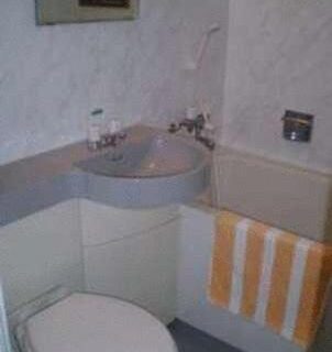 Compact bathroom with toilet, curved sink, mirror and striped towel at Ikawa Ryokan in Hiroshima