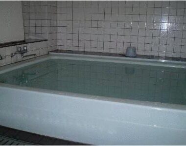 Indoor tiled soaking bath with filled basin and wall faucets at Ikawa Ryokan Hiroshima