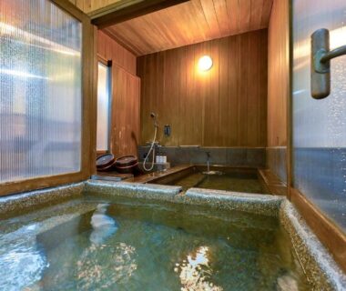 Indoor wooden onsen bath with tub, washing station and frosted windows at Ikkoten in Ōita, Kyūshū