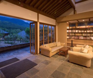 Ryokan lounge with sofas, bookshelf, stone floor and open doors to a garden courtyard and hillside view