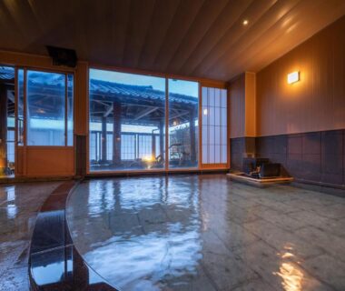 Warm indoor onsen bath with wooden ceiling and glass doors at Ikkyu -Seaside Hotel- in Yamagata