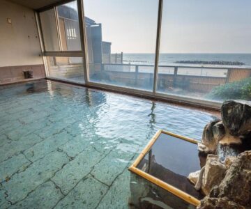 Indoor tiled onsen bath with large windows and sea beyond