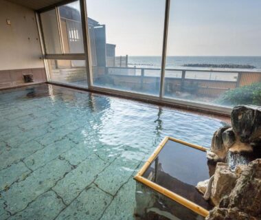 Indoor tiled onsen bath with large windows and sea beyond