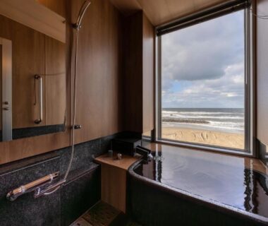 Wood-paneled bath with soaking tub and shower, window overlooking sandy beach, Ikkyu Seaside Hotel Yamagata