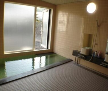 Tiled indoor onsen with rectangular soaking pool, shower stations and frosted window at Ikoiso Hokkaidō ryokan