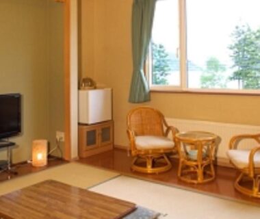 Tatami seating area with low table, rattan chairs and window view of trees at Ikoiso Hokkaidō