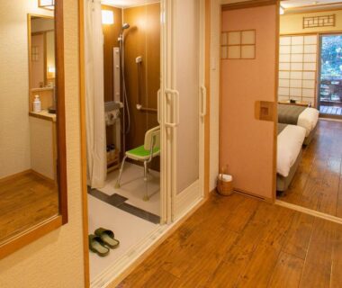 Wooden floored entryway leading to tatami room, compact wet-room shower and slippers by the doorway