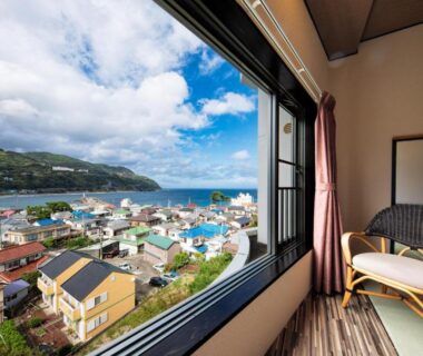 Sea and coastal village visible through large window with chair in room at Inatori Akao Hotel, Shizuoka