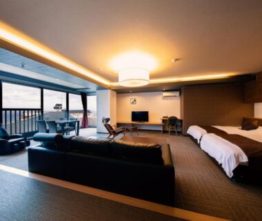 Spacious room with seating area, twin beds and floor-to-ceiling windows overlooking the coast at Inatori Akao Hotel Shizuoka