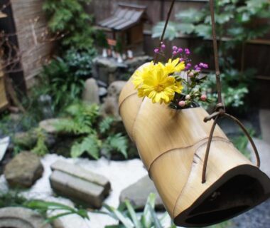 Bamboo spout with yellow flower above courtyard garden with stones and water basin at Inn Kawashima, Kyoto