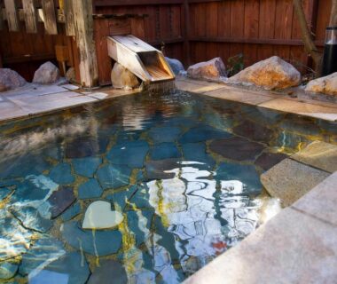 Outdoor stone onsen with wooden spout and rock edging at Innter Hill Tsubasa, Ōita