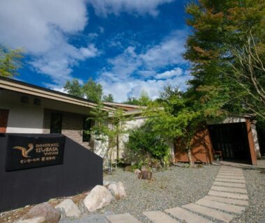 Stone walkway leading to ryokan entrance with wooden gate, landscaped trees and gravel courtyard in Yufuin Oita
