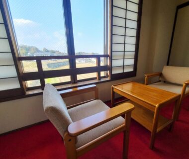 Two upholstered chairs and wooden table by shoji window overlooking countryside at Iris Yu, Iwate