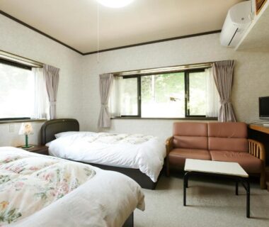 Two single beds, sofa and table in bright ryokan room with air conditioner and large windows